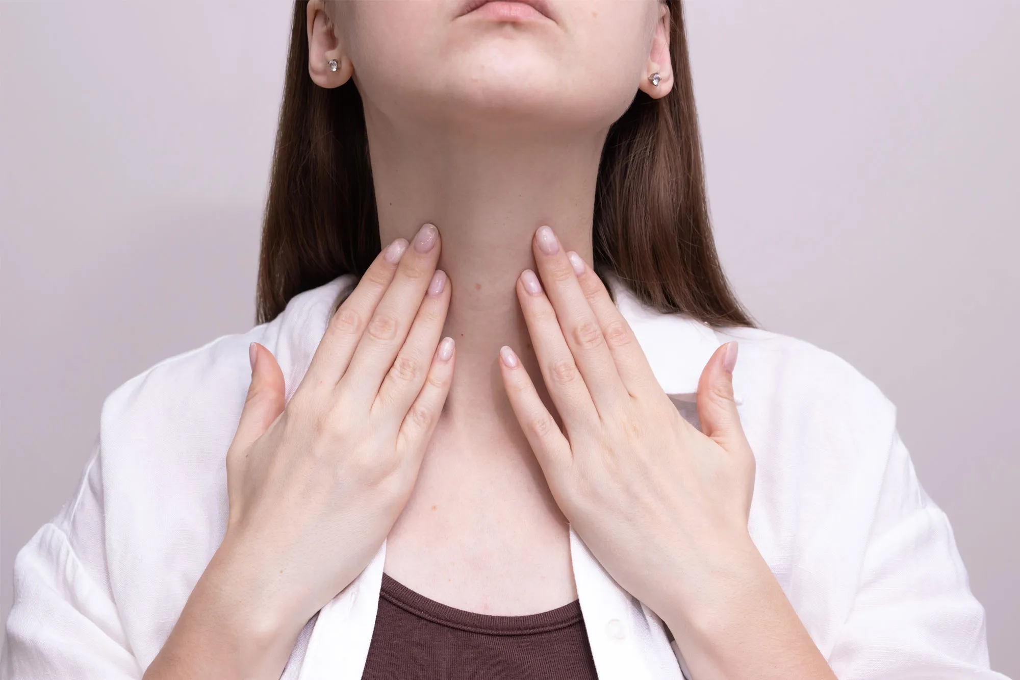 Young woman palpating her neck with her fingers, checking for swelling or discomfort.