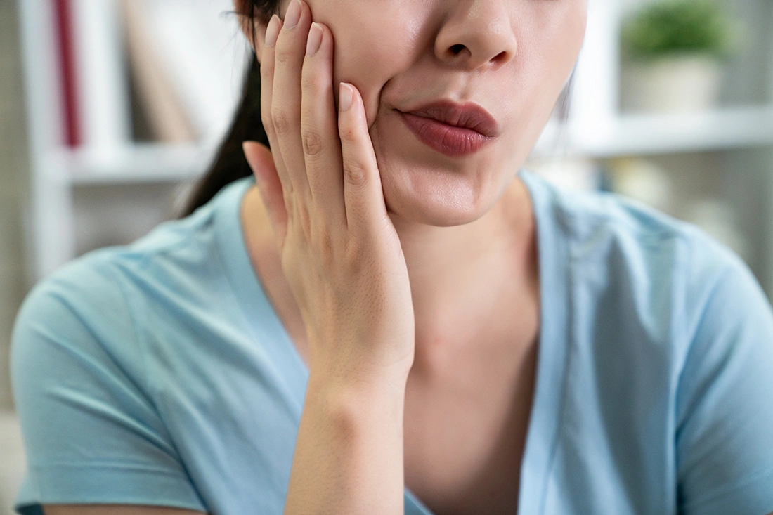 Woman touching the side of her face near the jaw, suggesting facial numbness or pain affecting the cheek and mouth area.