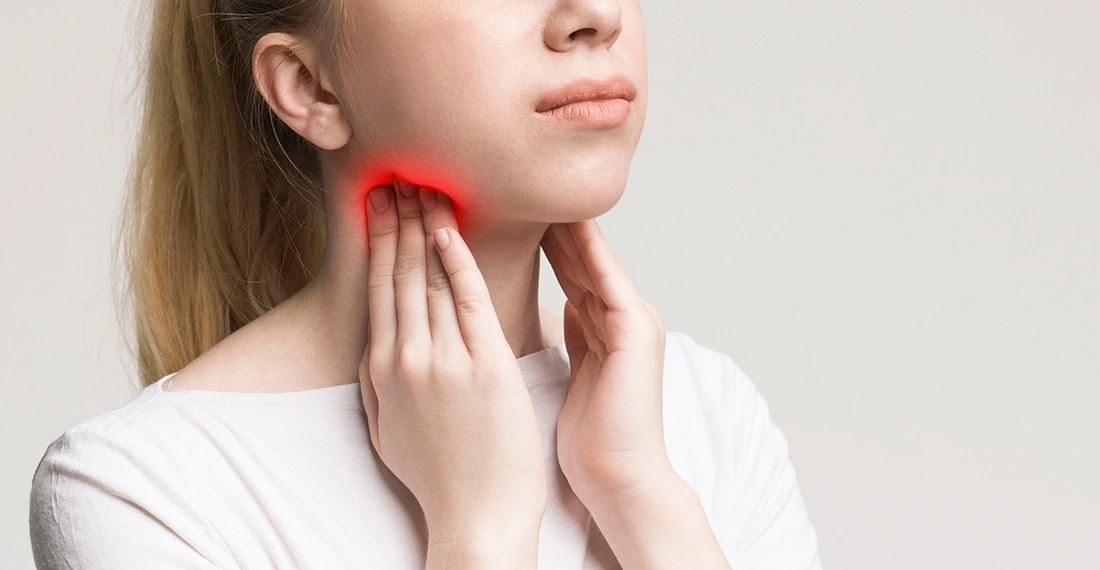 Woman touching the front of her neck where the thyroid gland is located, illustrating discomfort or concern related to thyroid problems.